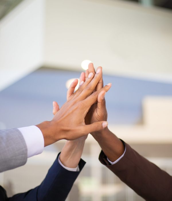 United business team celebrating success and joining hands. Group of three businesspeople giving high five to each other. Teambuilding concept
